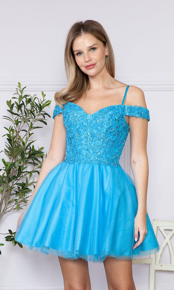 A woman indoors wears the Lace-Up Off-Shoulder Short Babydoll Hoco Dress9234 in Ocean Blue, featuring a lace-detailed bodice and flared tulle skirt. A plant is visible in the background.